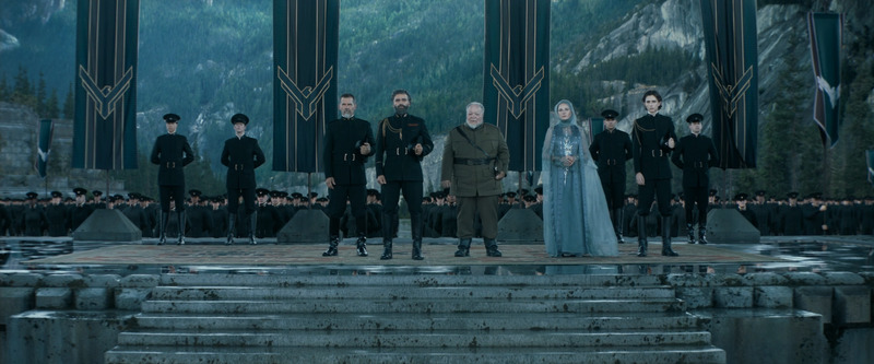 Duke Leto Atreides stands with his military and council. All dressed in military attire standing tall. 
Banners appear in the background with the Atreides symbol. Outdoors, separated from the lush environment by a stone platform.
